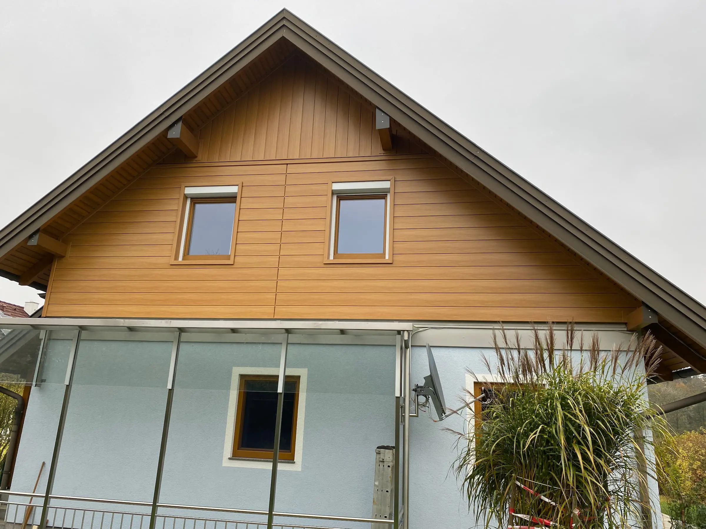 Fassadenelement aus Holz hellbraun mit zwei Fenstern, blaue Fassade darunter, Spenglerei Steyr Winterarbeit