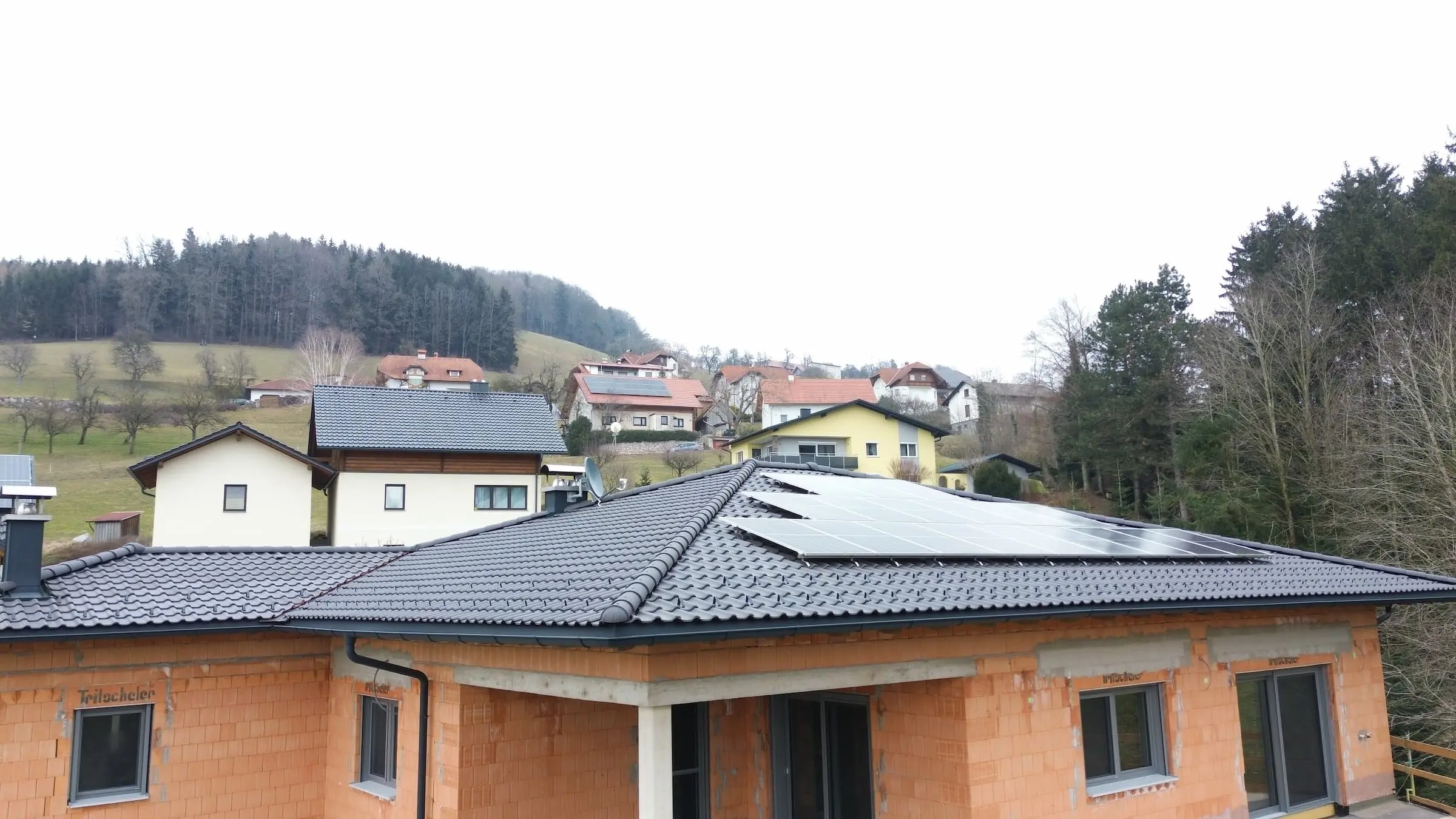 Dachdecker Steyr fertigt schwarzes Wienerberger Tondach mit Solarpaneelen auf Rohbau in ländlicher Umgebung