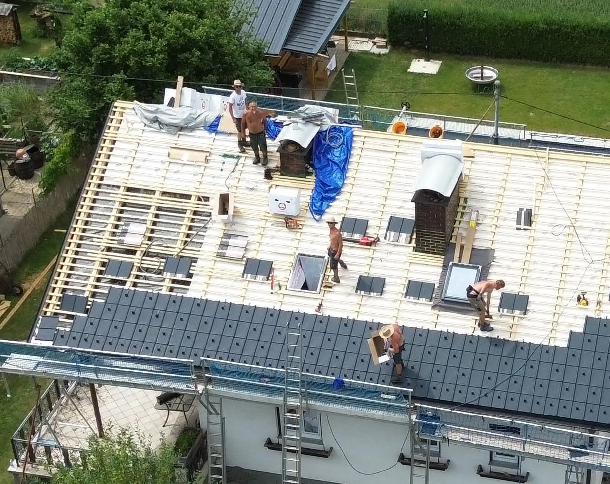 Dachdecker Steyr montieren graue Wienerberger Tondachziegel auf Holzlattung, Spenglerarbeiten am Schornstein sichtbar